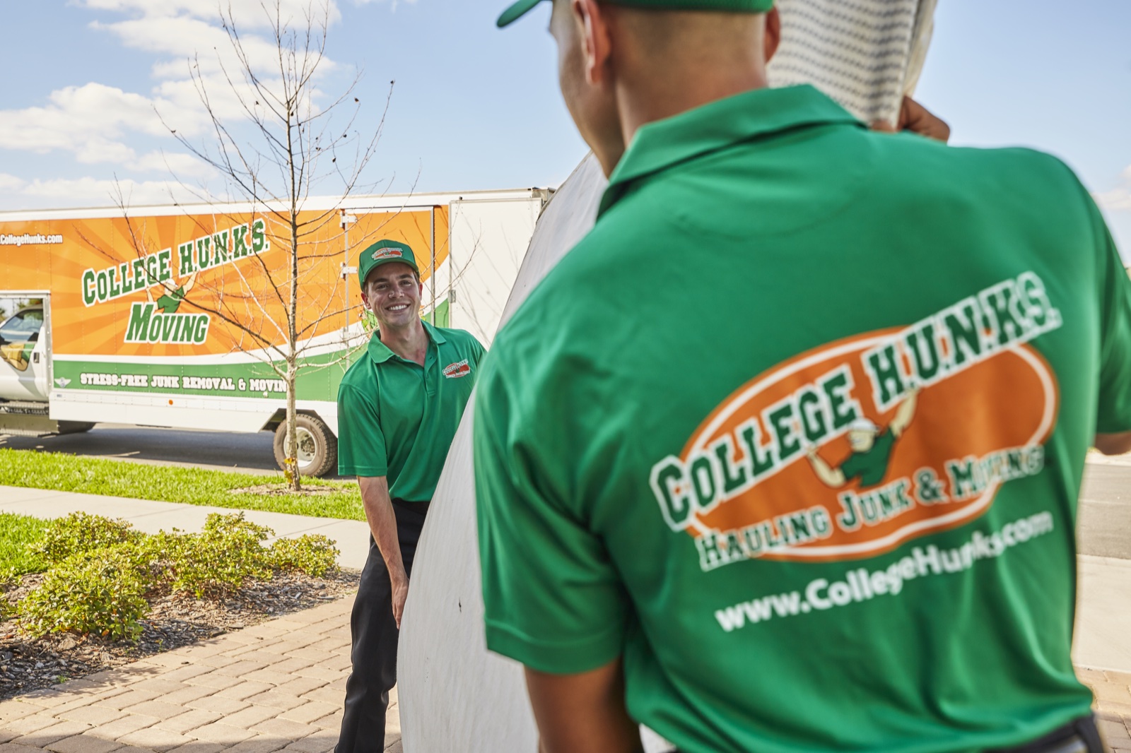 College HUNKS movers carrying furniture to a branded moving truck at a residential job