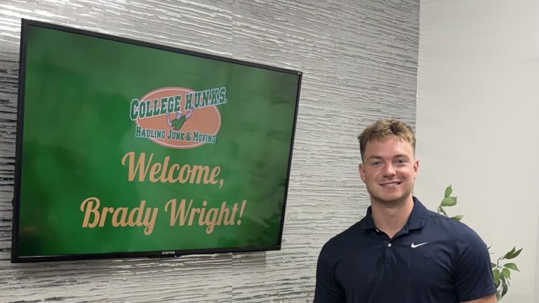Brady Wright next to a Welcome, Brady Wright! screen at College HUNKS headquarters in Tampa